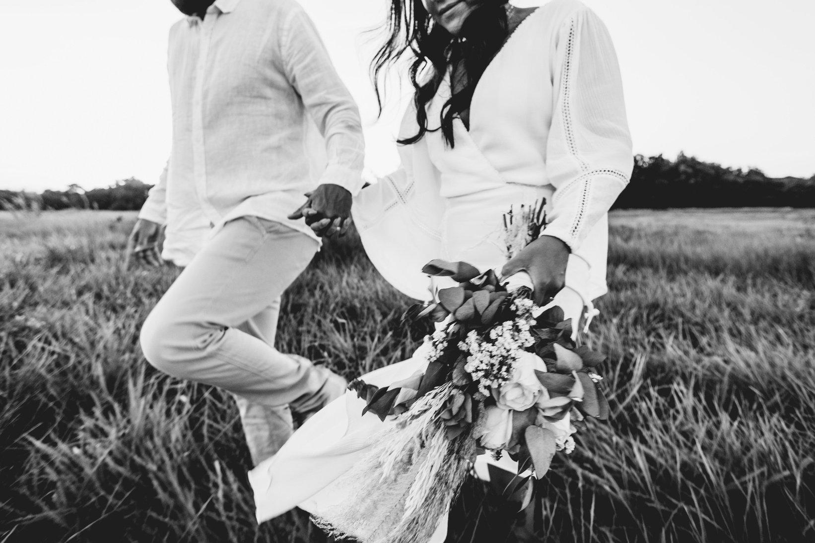 Crop newlywed couple with flower bouquet walking on meadow